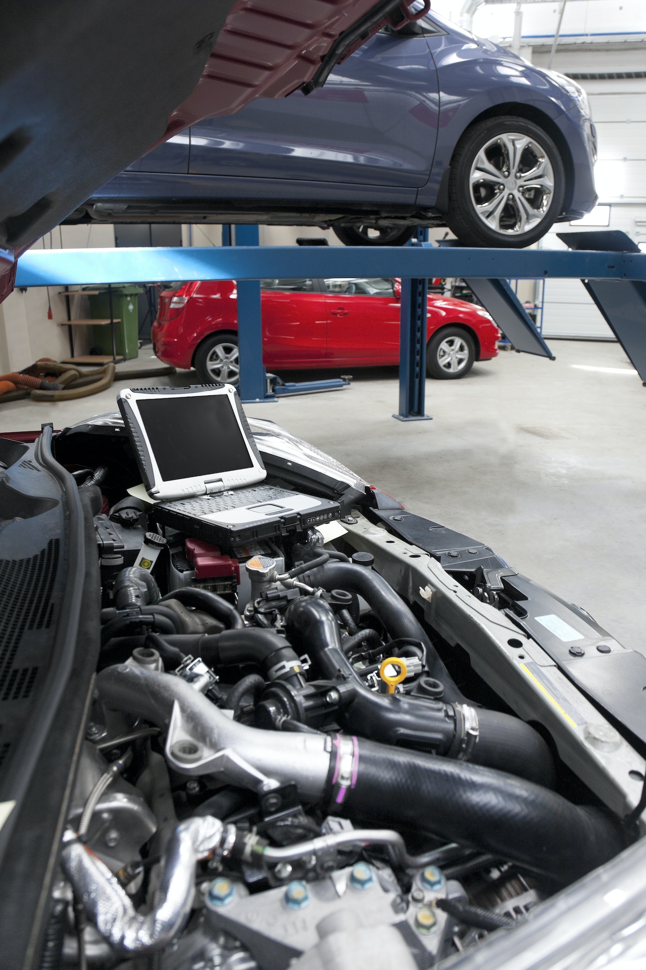 Car in a workshop and a computer running diagnostics on the engine.