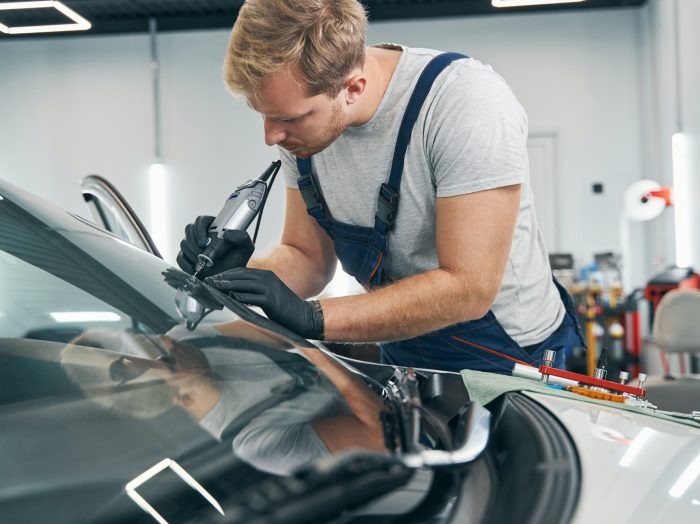Car service technician checks crack on car windshield closeup
