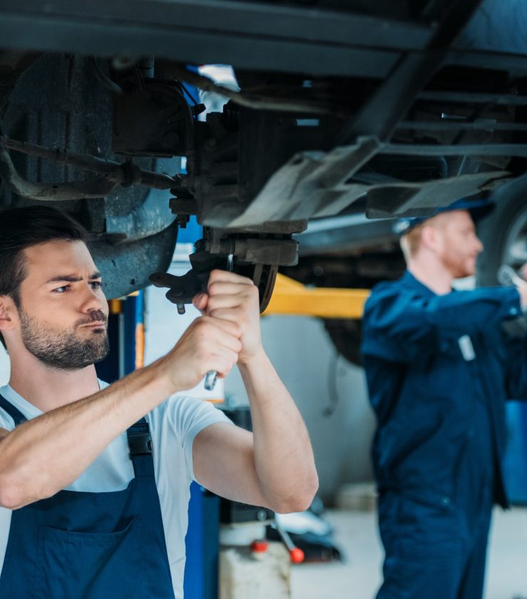 Two automechanics working on a car in a repair workshop.