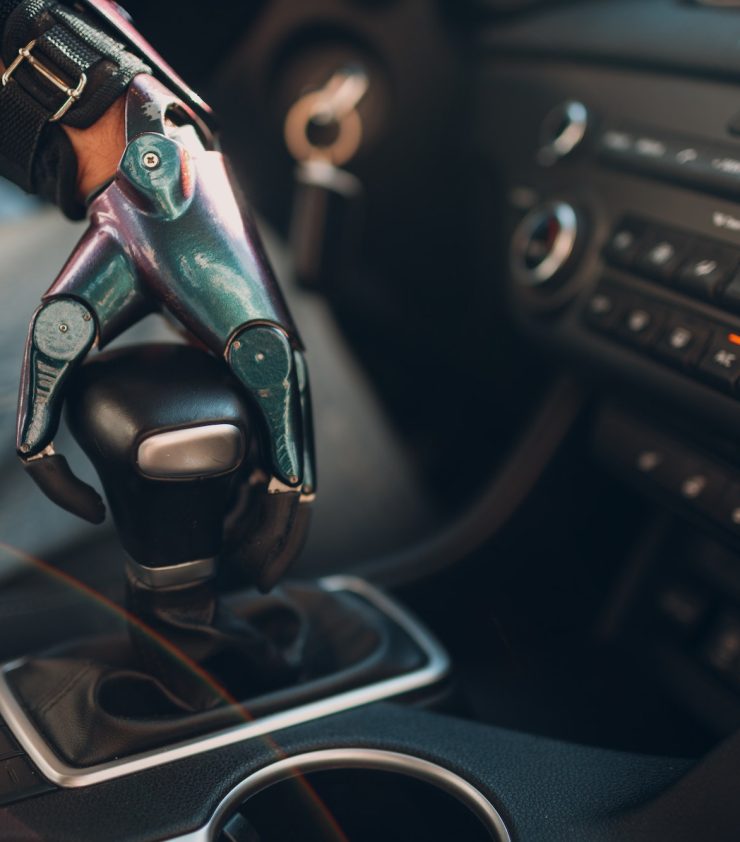 Young disabled man driver with artificial prosthetic hand driving vehicle car and switches gearbox.